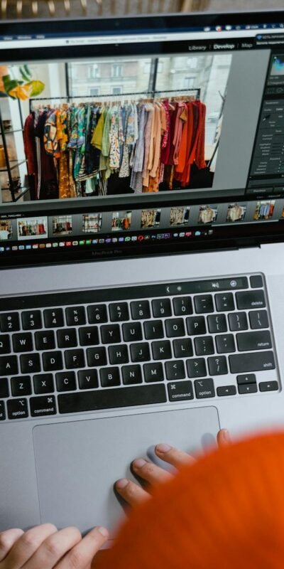 A person in a cozy setting edits photos of clothing displays on a laptop.