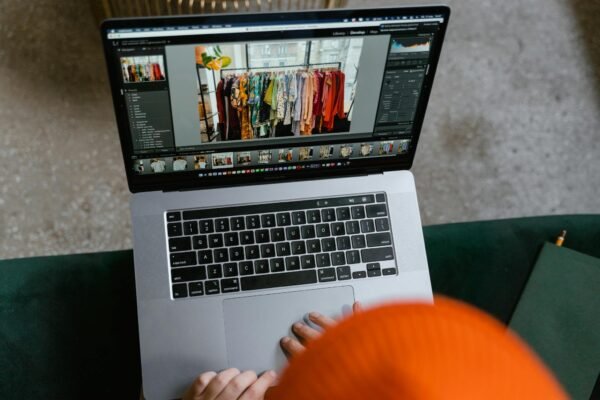 A person in a cozy setting edits photos of clothing displays on a laptop.