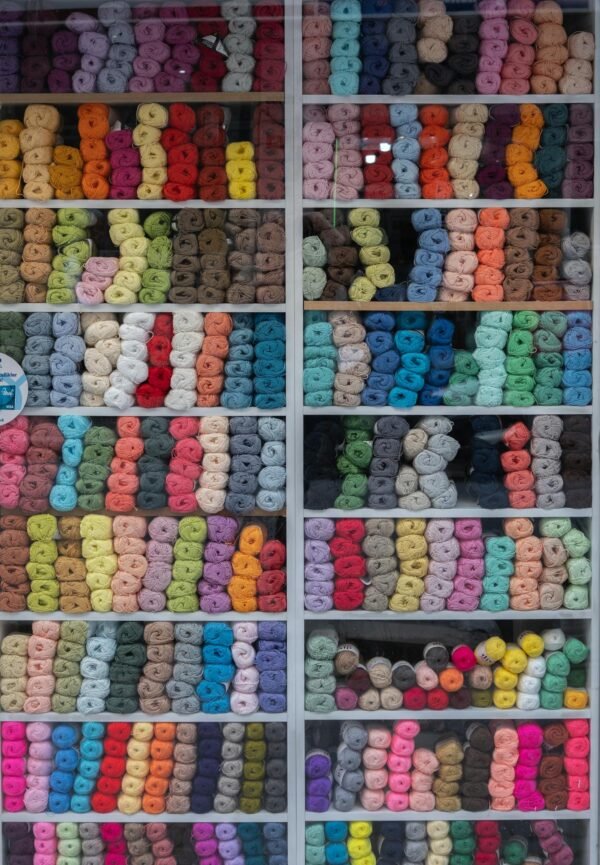 A vibrant display of various colored yarns arranged in neat rows on shelves, showcasing a wide range of materials and hues.