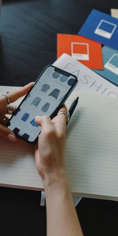 A woman browsing fashion items on a smartphone while sitting at a desk indoors.