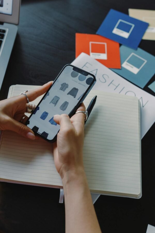 A woman browsing fashion items on a smartphone while sitting at a desk indoors.