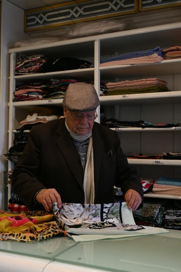 Elderly man attentively folding fabric in a well-organized textile store.